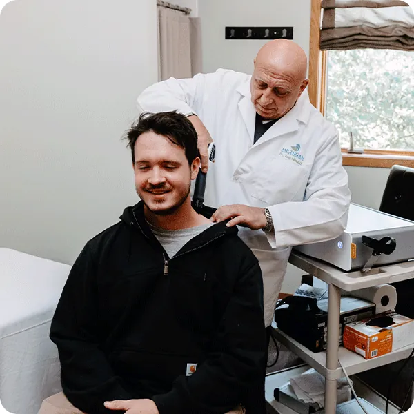 Doctor Tony applies shockwave therapy tool to male patient's neck and shoulder