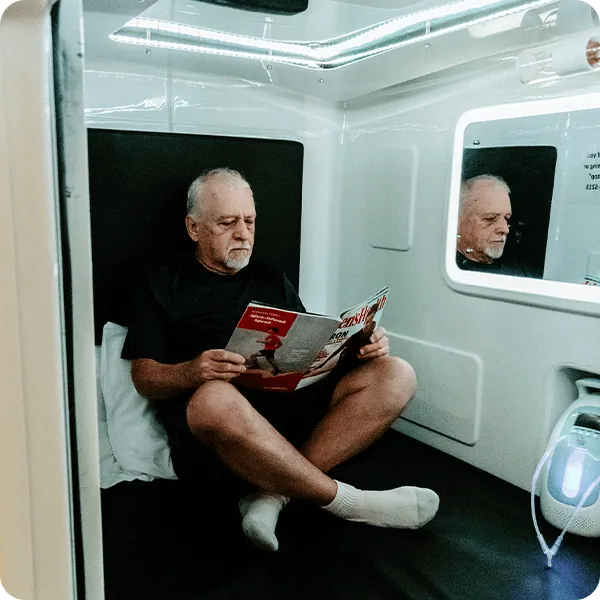 Male patient reading magazine while sitting in the Hyperbaric Cube Chamber